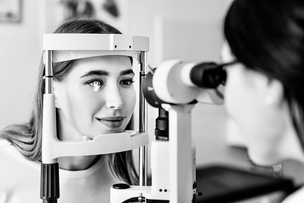 A woman undergoing an eye examination using a slit lamp, with the eye doctor focused on her eye through the instrument.