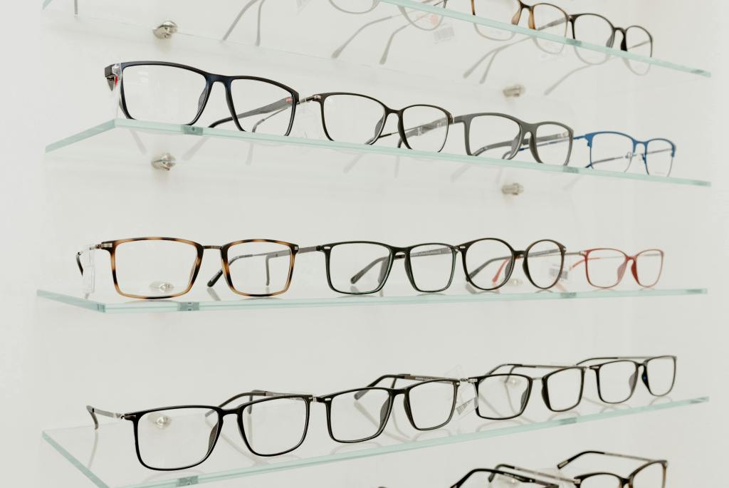 A variety of eyeglasses displayed on clear glass shelves in a retail store.