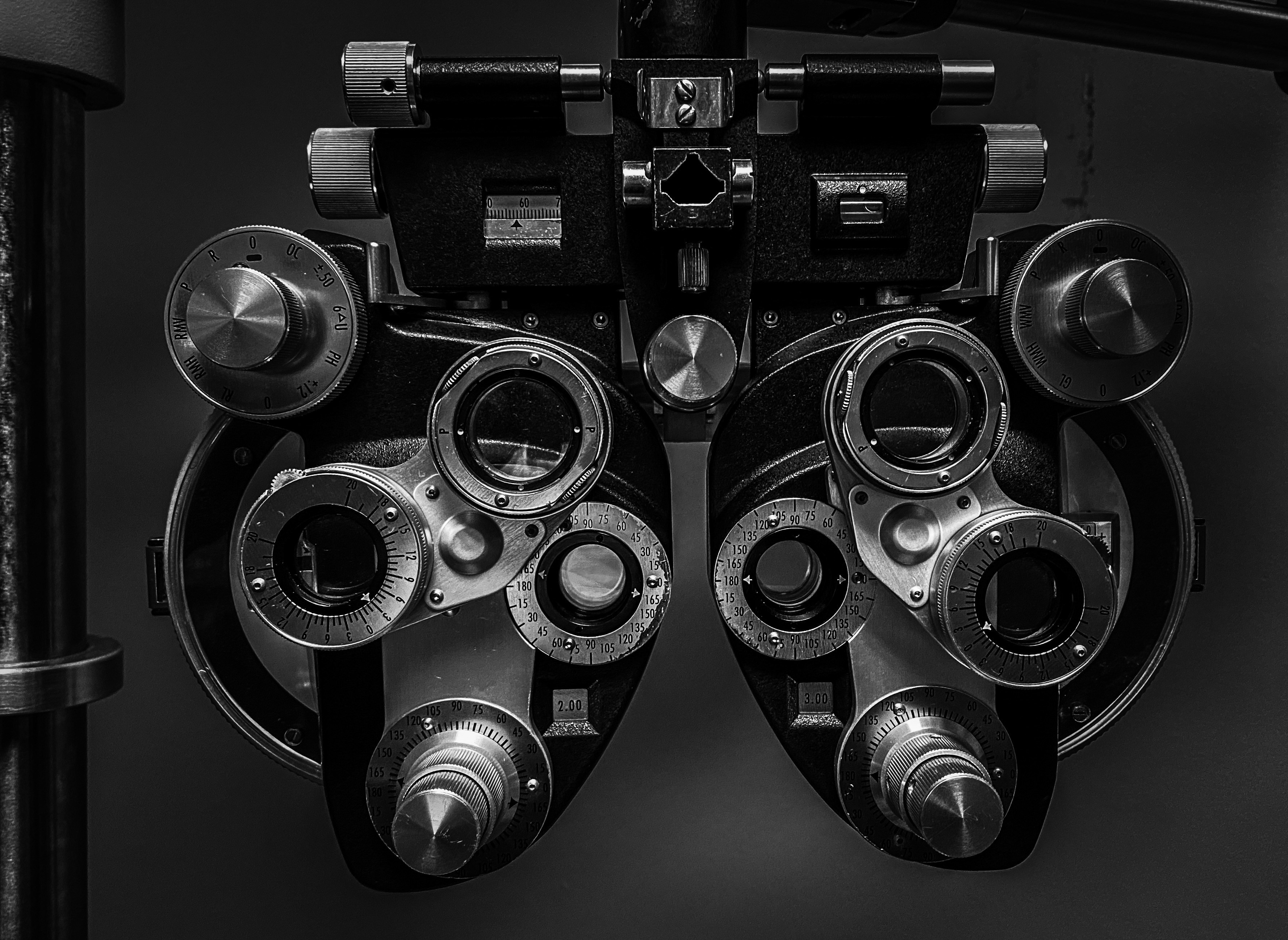 Close-up of a phoropter, an optical device used for vision testing, featuring various dials and lenses in black and white.